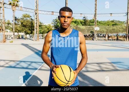Giocatore di basket maschile che tiene il basket in campo sportivo Foto Stock