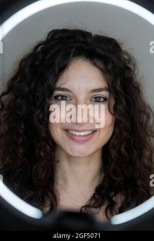 Donna sorridente con illuminatore anulare di fronte allo sfondo grigio Foto Stock