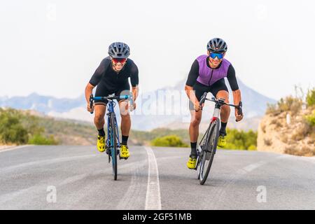Ciclisti maschi sorridenti che cavalcano le biciclette insieme su strada Foto Stock