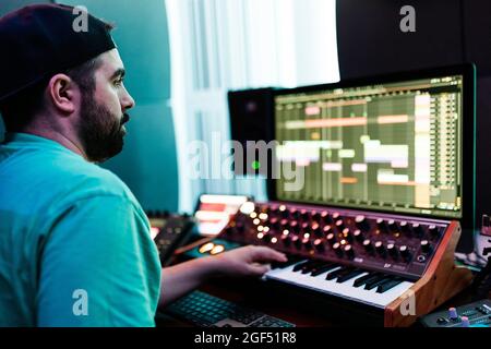 Artista maschile medio adulto che suona sintetizzatore mentre mixa il suono in studio Foto Stock