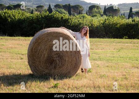 Giovane donna appoggiata su una balla di paglia durante la giornata di sole Foto Stock