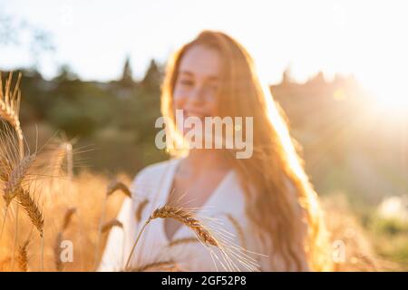 Piante di grano di fronte alla donna sorridente sul campo durante la giornata di sole Foto Stock