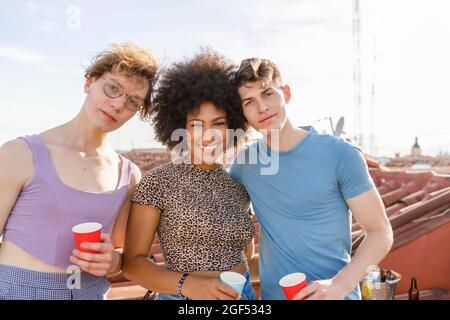 Giovani amici maschi e femmine che tengono tazze da drink usa e getta durante il party in terrazza Foto Stock