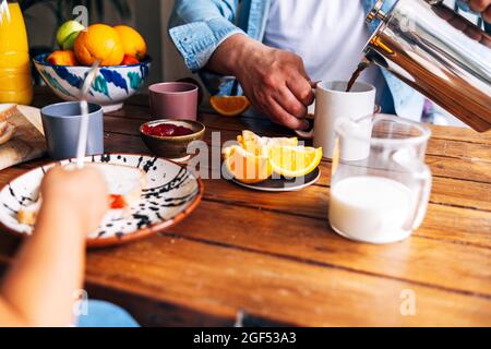 Uomo che versa il caffè in tazza mentre fa colazione con la figlia al tavolo Foto Stock