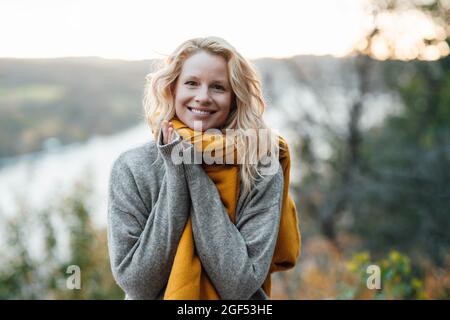 Donna bionda in maglione grigio sorridente al tramonto Foto Stock