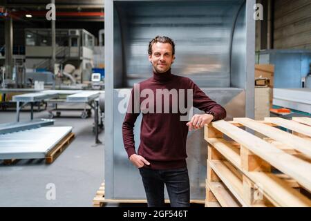 Professionale maschio con mano in tasca in piedi da una pila di pallet in legno Foto Stock
