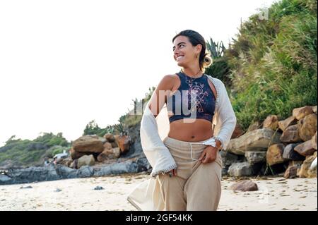Sorridente giovane donna che guarda via mentre corre in spiaggia Foto Stock