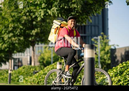 Felice uomo di consegna che guarda via mentre si guida in bicicletta durante la giornata di sole Foto Stock