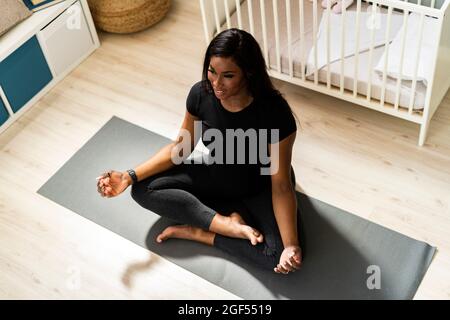 Sorridente giovane donna incinta che fa yoga mentre si siede sul tappeto a casa Foto Stock