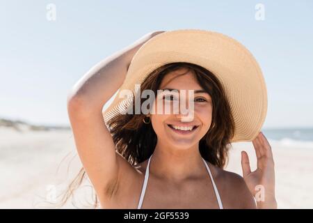 Bella donna in cappello di sole sorridente mentre si gode in spiaggia Foto Stock