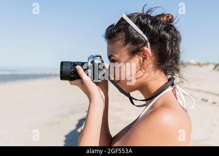 Donna che fotografa attraverso la macchina fotografica in spiaggia il giorno di sole Foto Stock