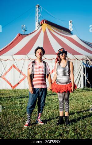 Clown maschio e femmina che tiene le mani mentre si trova di fronte alla tenda del circo Foto Stock