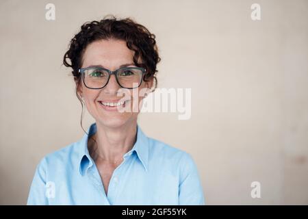 Donna d'affari sorridente che indossa occhiali in piedi di fronte al muro Foto Stock