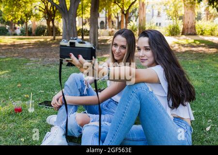 Donne che prendono selfie attraverso la macchina fotografica mentre si siedono al parco pubblico Foto Stock