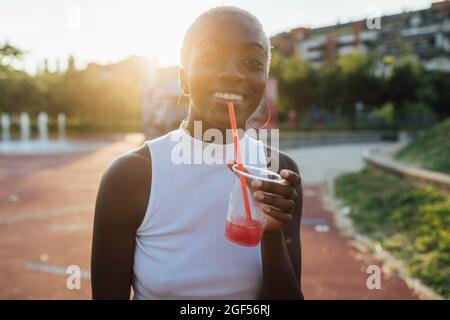Donna sorridente che tiene il frullato mentre si alza al parco Foto Stock