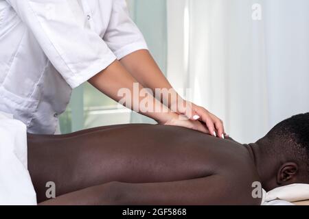 donna massaggiatrice che fa il massaggio della zona posteriore all'uomo nero Foto Stock