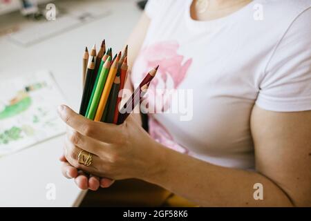 un mazzo di matite colorate nelle mani della donna , una scrivania con disegni sullo sfondo Foto Stock