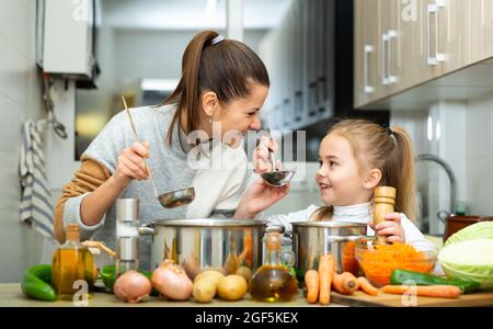 Felice madre giovane e figlia degustazione zuppa di verdure Foto Stock