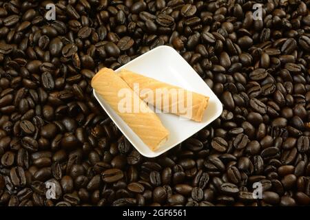Caffè panna wafer rotoli biscotti su snack piatto bianco su chicchi di caffè Foto Stock