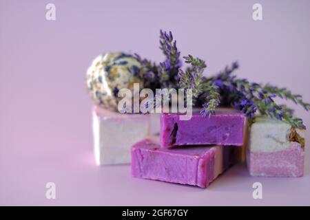 Sapone lavanda e bombe da bagno, ciuffi di lavanda su sfondo viola chiaro. Cosmetici vegani eco-compatibili . Cosmetici biologici a base di erbe con lavanda Foto Stock