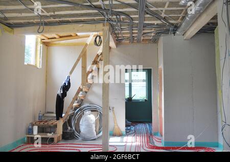 Una vista dall'interno della casa in costruzione con soffitto isolato in vetroresina, cablaggio elettrico interno in tubo metallico, muro a secco, acqua calda sotto Foto Stock