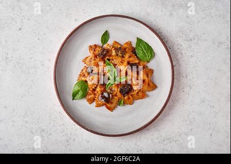 Farfalle di pasta con melanzane, salsa di pomodoro, formaggio e basilico sul piatto su sfondo grigio, vista dall'alto, da vicino Foto Stock