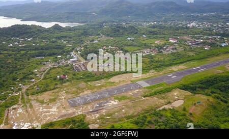 Vista della pista dell'aeroporto circondata dalla città di Labuan Bajo. Foto Stock