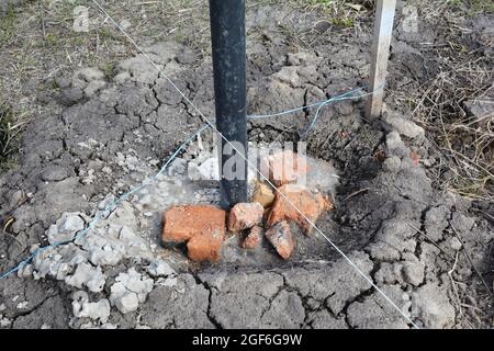 Un primo piano su un'installazione di palo di metallo della recinzione, mettendo in calcestruzzo usando una linea piana o una corda, ghiaia schiacciata, mattoni rotti e calcestruzzo per riempire il th Foto Stock