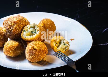 palle di formaggio con aneto interno per uno spuntino in un piatto su sfondo nero. Foto Stock