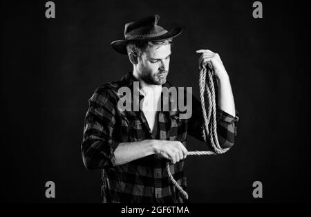 canottaggio nato. rodeo selvaggio west. uomo su fondo nero cappello. cowboy con corda di lasso. Western. Uomo camicia a scacchi sul ranch. Uomo in stile vintage. Ovest selvaggio Foto Stock