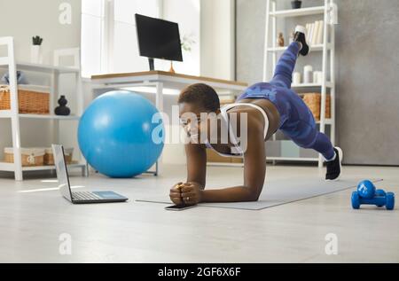 Donna che fa esercizi sportivi di fronte al laptop durante la trasmissione online di allenamento fitness. Foto Stock