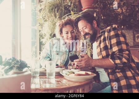 Coppia felice adulto godere bar ristorante pausa tempo libero al coperto con l'uso moderno cellulare per videochiamare gli amici o alla ricerca di on-line Foto Stock