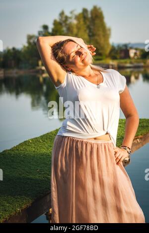 Ritratto di attraente donna più grande godendo la luce del sole in caldo giorno d'estate. Corpo positivo. Bella donna caucasica sovrappeso indossando gonna all'aperto Foto Stock
