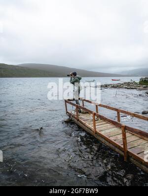 Escursionista fotografato su un ponte di legno sopra il lago Leitisvatn, Vagar, Isole Faroe Foto Stock