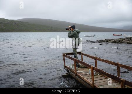 Escursionista fotografato su un ponte di legno sopra il lago Leitisvatn, Vagar, Isole Faroe Foto Stock