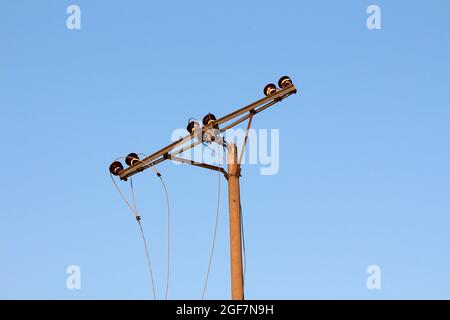 Il vecchio palo per utenze elettriche in calcestruzzo dilapidato è stretto con supporto in metallo ritorto danneggiato per sei isolatori in ceramica incrinati sulla parte superiore Foto Stock