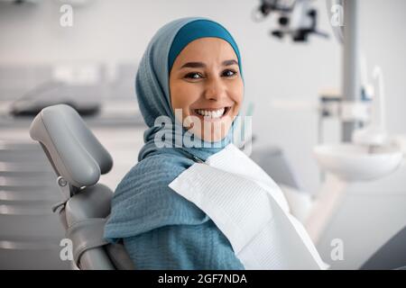 Trattamento stomatologico. Felice giovane donna islamica in Hijab seduta in sedia dentisti Foto Stock
