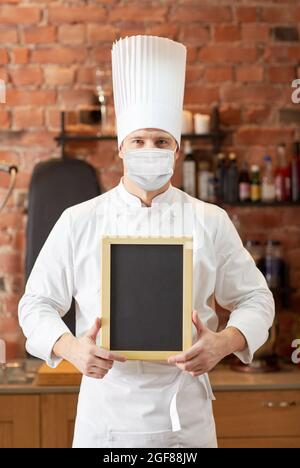 chef maschile in maschera con menù nero gesso bordo Foto Stock