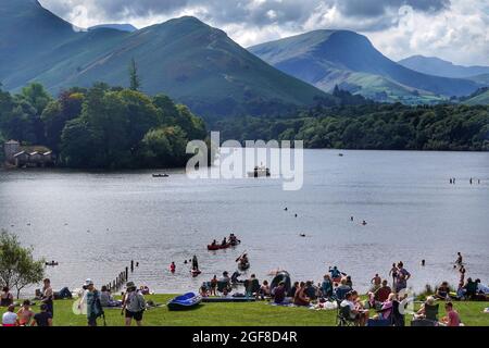 La folla si prende il sole a Crow Park sulle rive di Derwentwater nel Lake District mentre i visitatori di Cumbria sono invitati a prendere un test di flusso laterale prima di viaggiare per la contea dopo un forte aumento dei casi di coronavirus nella regione. Data foto: Martedì 24 agosto 2021. Foto Stock