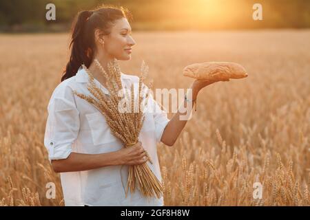 Donna che tiene in mano pane di grano fatto in casa e Spago di orecchie in campo di grano al Tramonto Foto Stock