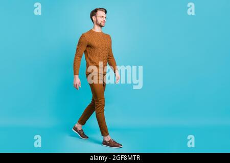 Foto di carino dolce giovane Signore indossare occhiali marrone pullover camminare guardando spazio vuoto sorridente isolato blu sfondo di colore Foto Stock