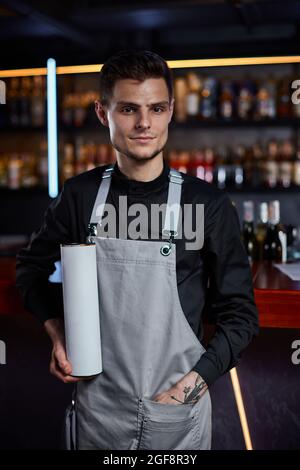 Bel barman in grembiule in piedi al bancone bar Foto Stock