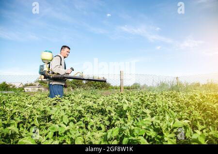 Un agricoltore con una macchina spruzzatrice di pesticidi attraversa il campo. Protezione di piante da insetti e infezioni fungine. Industria chimica in farmina Foto Stock