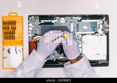 Vista dall'alto di un tecnico con guanti bianchi, che fissa un laptop a un tavolo bianco Foto Stock