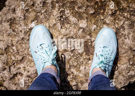 I piedi da donna in sneakers blu si erono su una pietra Foto Stock