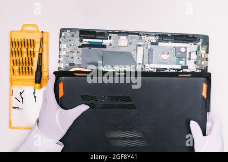 Vista dall'alto di un tecnico con un guanto bianco, rimuovendo il coperchio di un laptop prima di essere riparato su un tavolo bianco Foto Stock