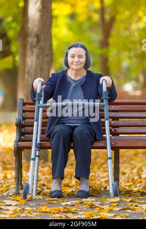 Donna con camminatore seduto su panchina nel parco autunnale Foto Stock