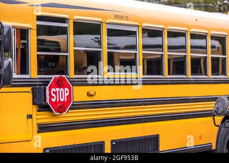 Un primo piano di un autobus scolastico giallo arancione con un cartello rosso per tornare a scuola Foto Stock