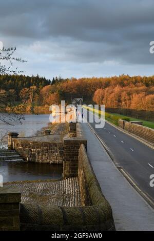 Diga argine muro, camminatori su strada, autunnale legno colori, scuro autunno sera cielo - Fewston Reservoir, Washburn Valley, Yorkshire, Inghilterra Regno Unito. Foto Stock