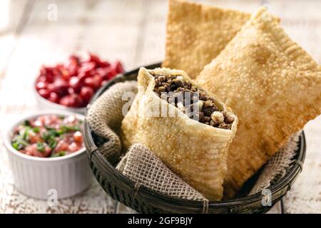 Pasta fritta ripiena di carne macinata e patate, salsa calda servita calda. Foto Stock